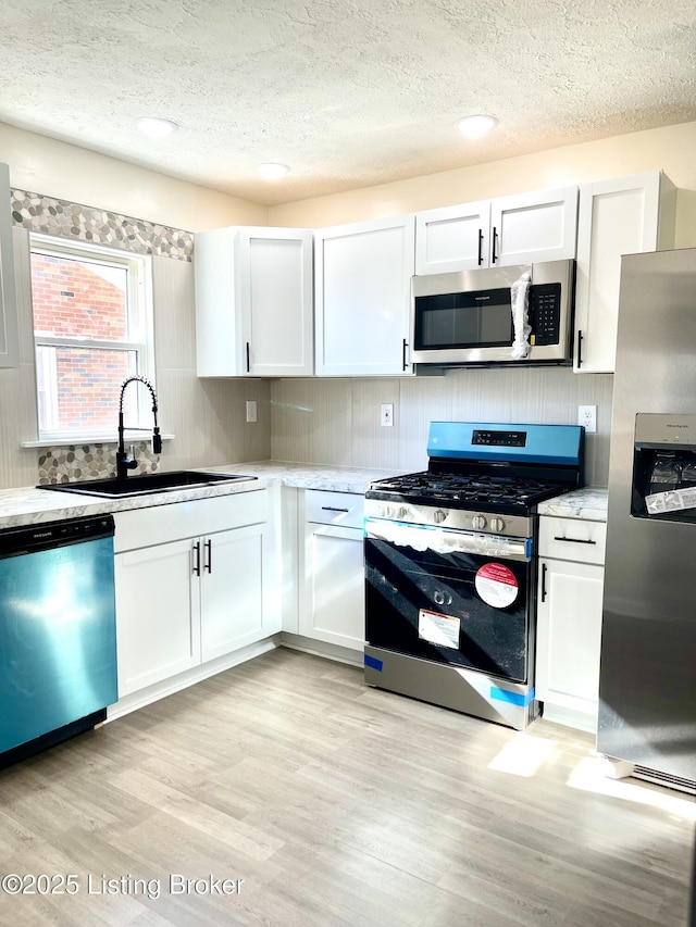 kitchen featuring sink, appliances with stainless steel finishes, tasteful backsplash, white cabinets, and light wood-type flooring