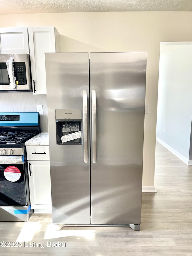 kitchen featuring white cabinetry, appliances with stainless steel finishes, light stone counters, and light hardwood / wood-style floors