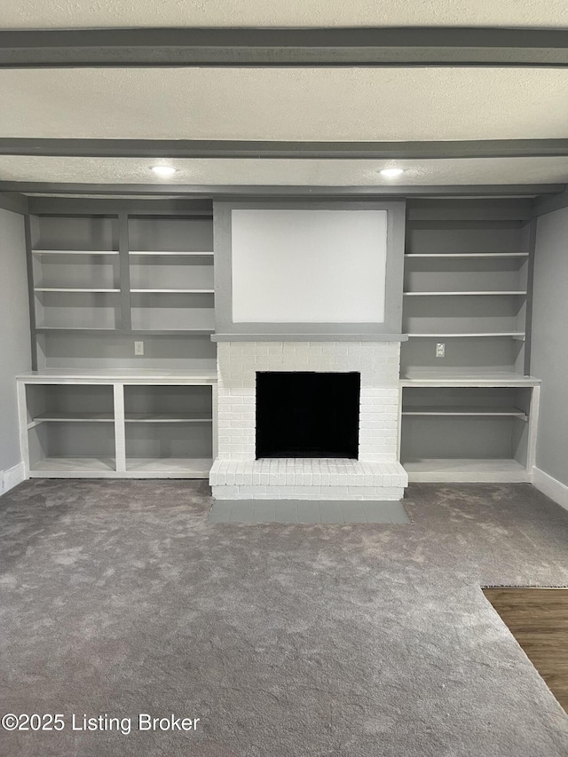 unfurnished living room with built in features, a fireplace, dark colored carpet, a textured ceiling, and beam ceiling