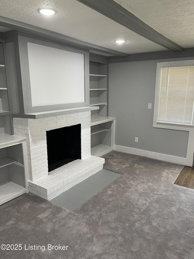 unfurnished living room featuring a brick fireplace, beam ceiling, a textured ceiling, and dark colored carpet