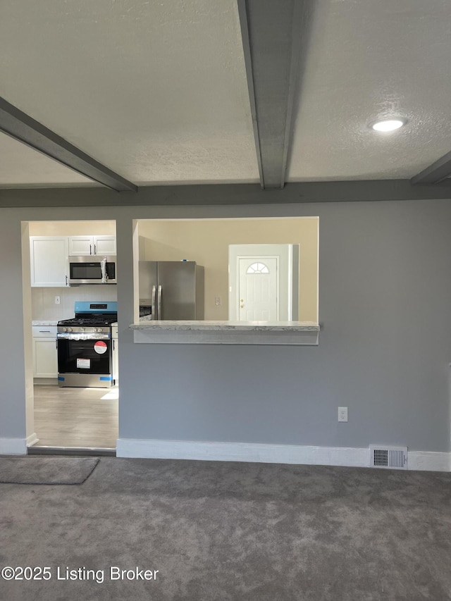 interior space featuring a textured ceiling, beamed ceiling, and carpet