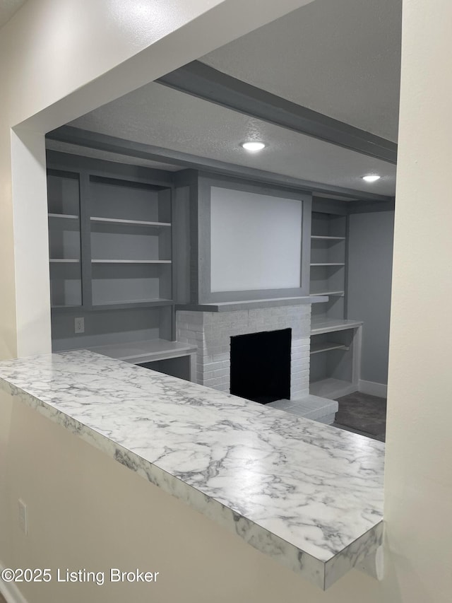 interior space with beam ceiling, built in shelves, a fireplace, and a textured ceiling