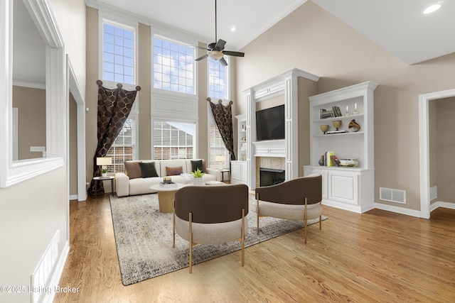 living room featuring ceiling fan, ornamental molding, a towering ceiling, and light hardwood / wood-style floors