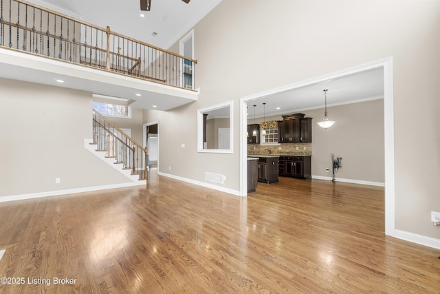 unfurnished living room featuring a towering ceiling, wood-type flooring, ornamental molding, and ceiling fan