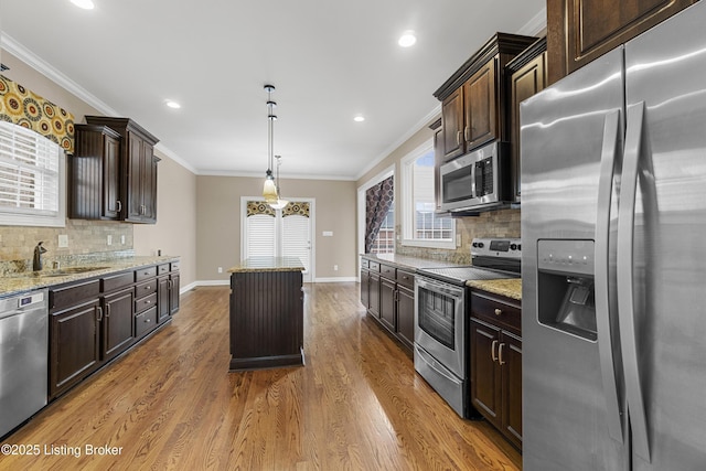 kitchen featuring sink, crown molding, hanging light fixtures, stainless steel appliances, and light stone counters