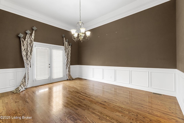 empty room with french doors, ornamental molding, wood-type flooring, and a chandelier