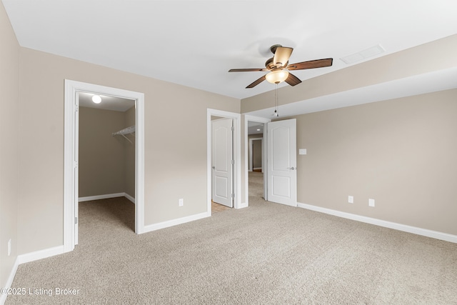 unfurnished bedroom featuring ceiling fan, a closet, a spacious closet, and light carpet