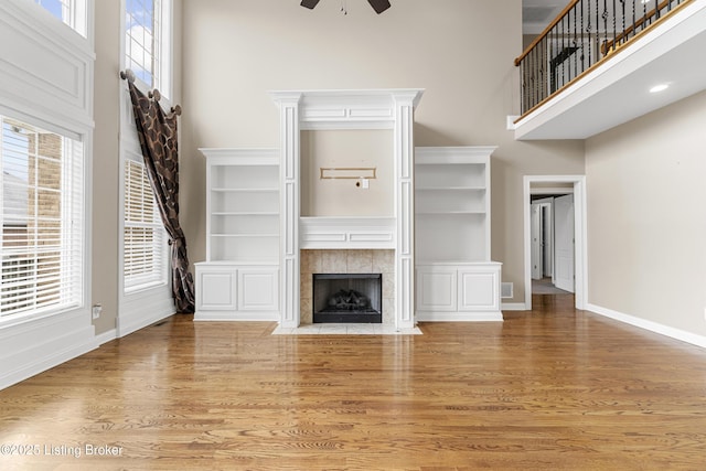 unfurnished living room featuring hardwood / wood-style flooring, a towering ceiling, a tiled fireplace, and ceiling fan