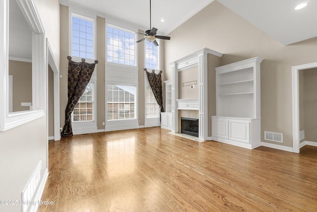 unfurnished living room with built in features, a high ceiling, ornamental molding, ceiling fan, and light hardwood / wood-style flooring