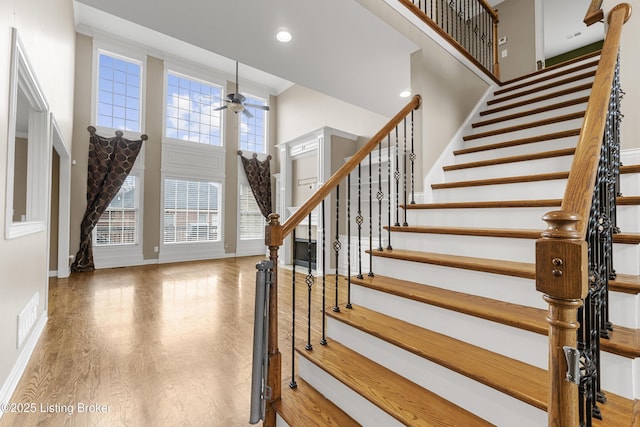 staircase with a high ceiling, hardwood / wood-style floors, and ceiling fan