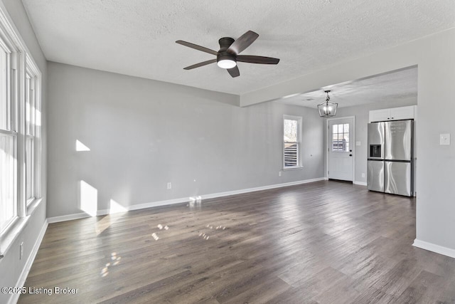 unfurnished living room with dark wood-type flooring, ceiling fan with notable chandelier, and a textured ceiling