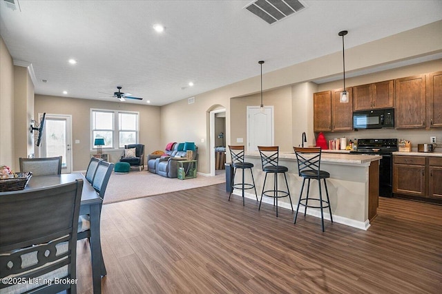 kitchen with pendant lighting, dark hardwood / wood-style flooring, a kitchen breakfast bar, a center island, and black appliances