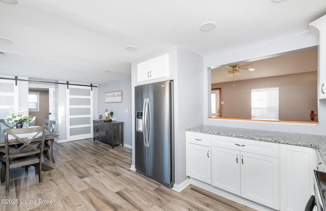 kitchen featuring stainless steel refrigerator with ice dispenser, light stone countertops, white cabinets, a barn door, and light wood-type flooring