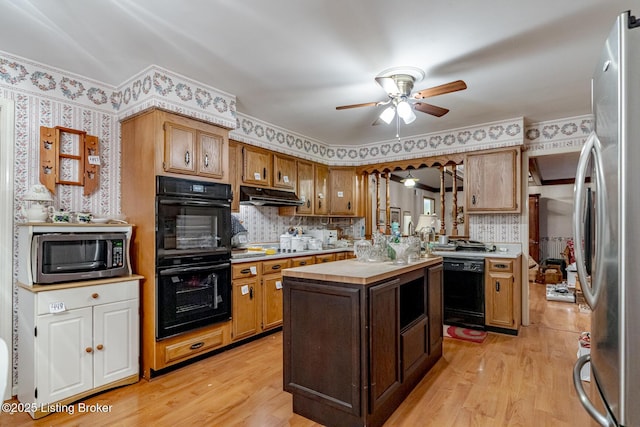 kitchen with backsplash, a center island, ceiling fan, black appliances, and light hardwood / wood-style flooring