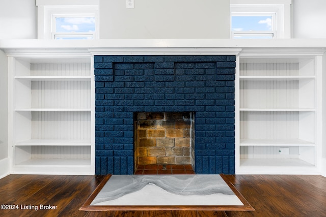 room details with built in shelves, hardwood / wood-style floors, and a brick fireplace