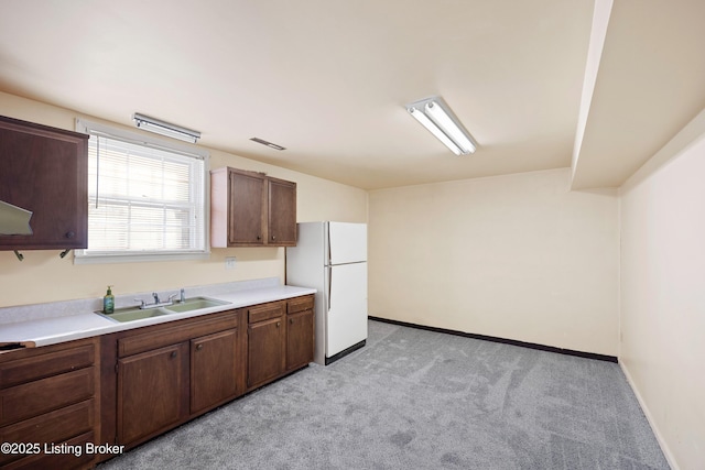 kitchen with dark brown cabinetry, sink, light colored carpet, and white refrigerator