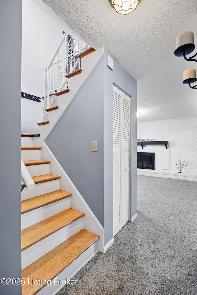 stairway featuring a brick fireplace, carpet floors, and a textured ceiling