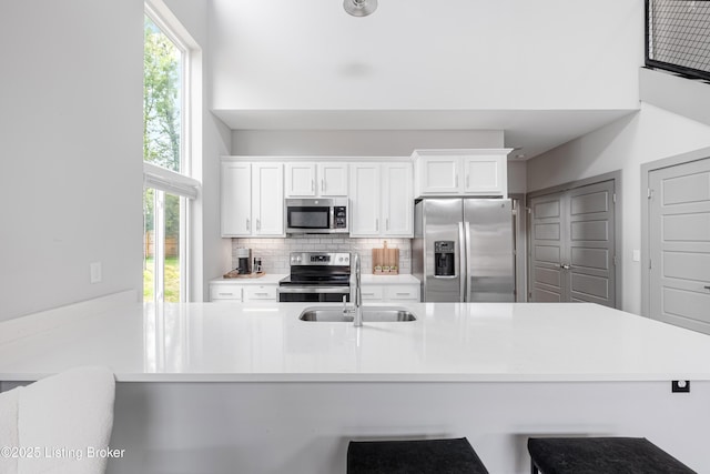 kitchen with sink, a breakfast bar area, appliances with stainless steel finishes, white cabinets, and decorative backsplash