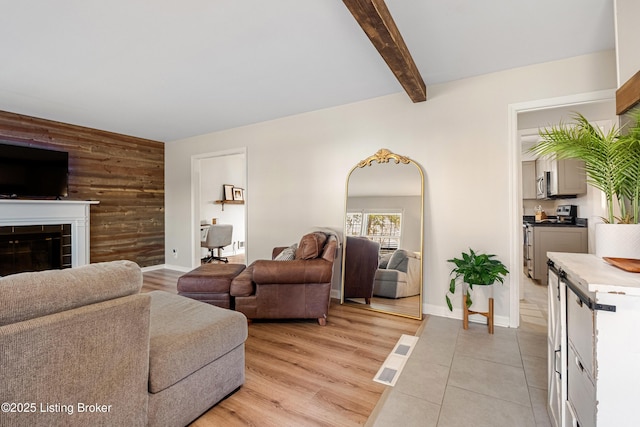 living room with beamed ceiling, a tile fireplace, wooden walls, and light hardwood / wood-style floors