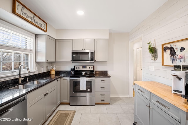 kitchen with light tile patterned flooring, sink, gray cabinetry, dark stone countertops, and appliances with stainless steel finishes