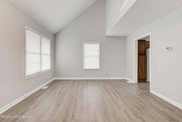 spare room with light hardwood / wood-style flooring, a textured ceiling, and vaulted ceiling