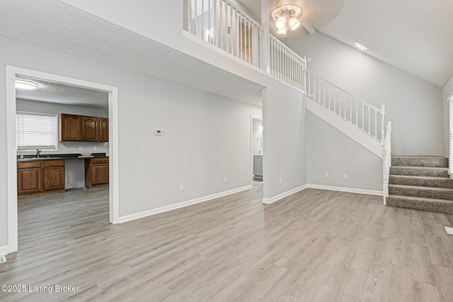 unfurnished living room featuring sink, a towering ceiling, light hardwood / wood-style floors, and a textured ceiling