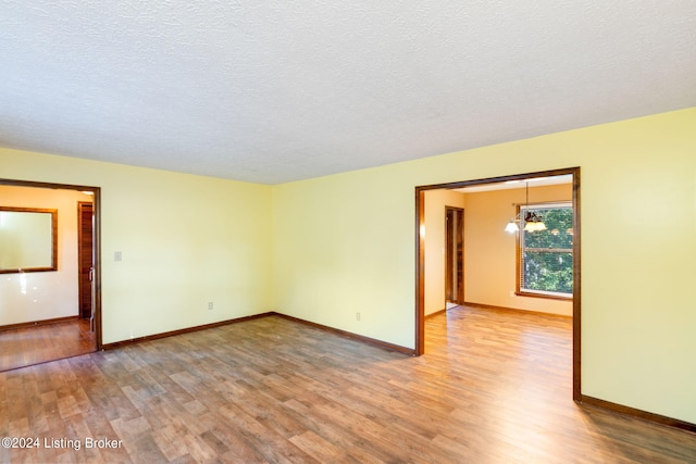 empty room with hardwood / wood-style flooring, a notable chandelier, and a textured ceiling