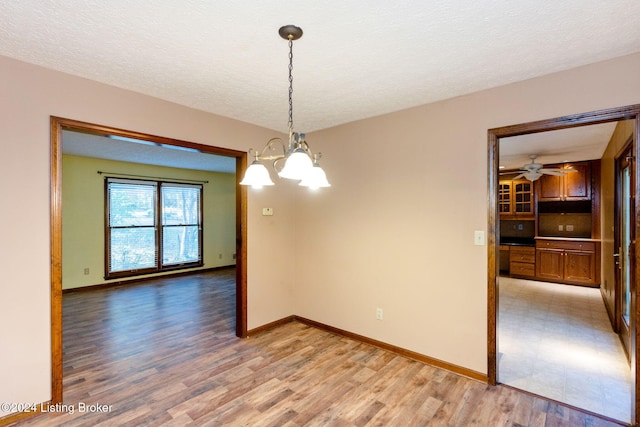 unfurnished dining area with light hardwood / wood-style floors, a textured ceiling, and a notable chandelier