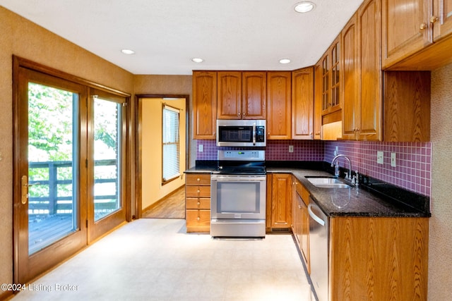 kitchen with backsplash, appliances with stainless steel finishes, sink, and dark stone counters