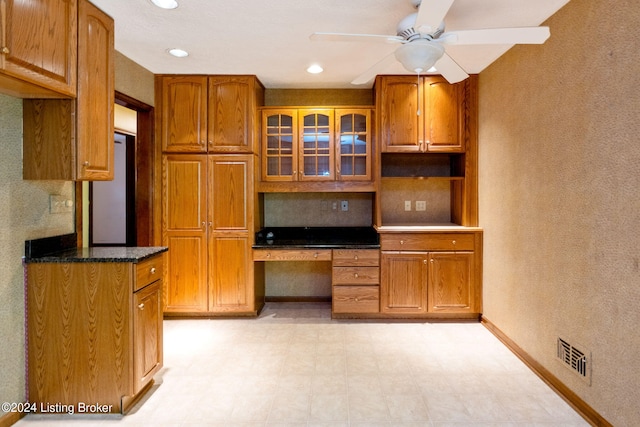 kitchen featuring ceiling fan, refrigerator, tasteful backsplash, built in desk, and dark stone counters