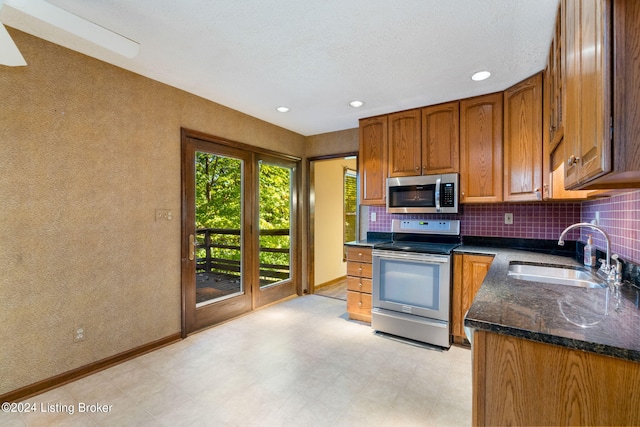 kitchen with tasteful backsplash, appliances with stainless steel finishes, sink, and dark stone counters