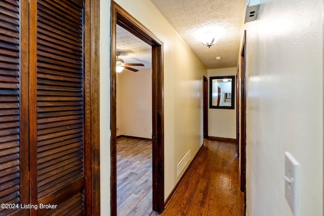 corridor with dark hardwood / wood-style flooring and a textured ceiling