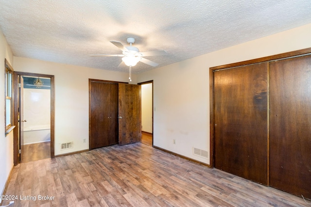 unfurnished bedroom with ceiling fan, hardwood / wood-style floors, a textured ceiling, and two closets