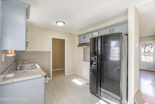 kitchen featuring black fridge, light hardwood / wood-style floors, sink, and backsplash