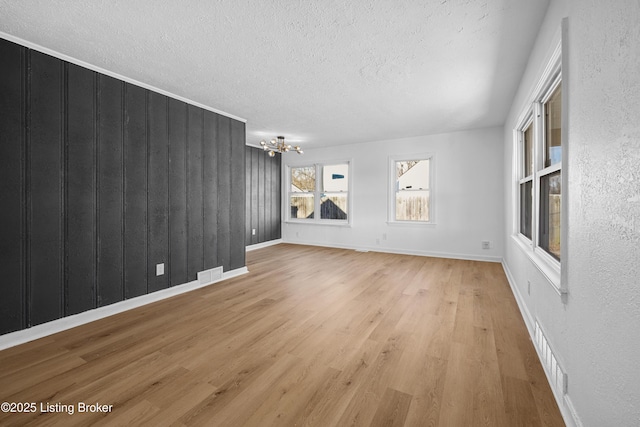 unfurnished living room with a chandelier, a textured ceiling, and light wood-type flooring