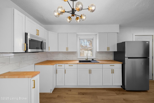 kitchen with stainless steel appliances, white cabinetry, pendant lighting, and wood counters