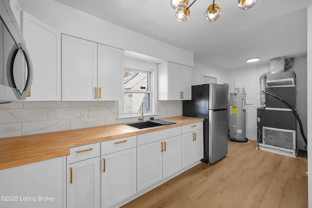 kitchen with appliances with stainless steel finishes, wood counters, white cabinetry, sink, and electric water heater