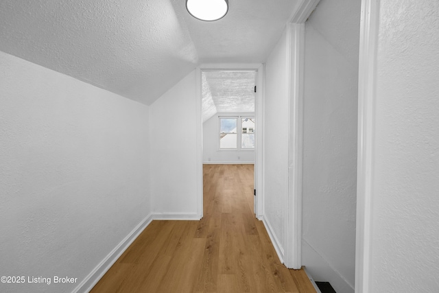 hall with vaulted ceiling, a textured ceiling, and light hardwood / wood-style flooring