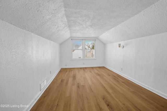 bonus room with vaulted ceiling, light hardwood / wood-style floors, and a textured ceiling