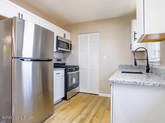 kitchen with sink, white cabinetry, stainless steel appliances, light stone counters, and light hardwood / wood-style floors