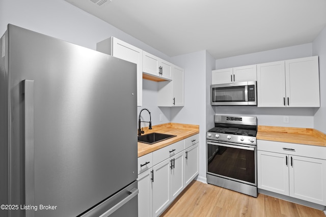 kitchen with white cabinetry, sink, butcher block countertops, and appliances with stainless steel finishes