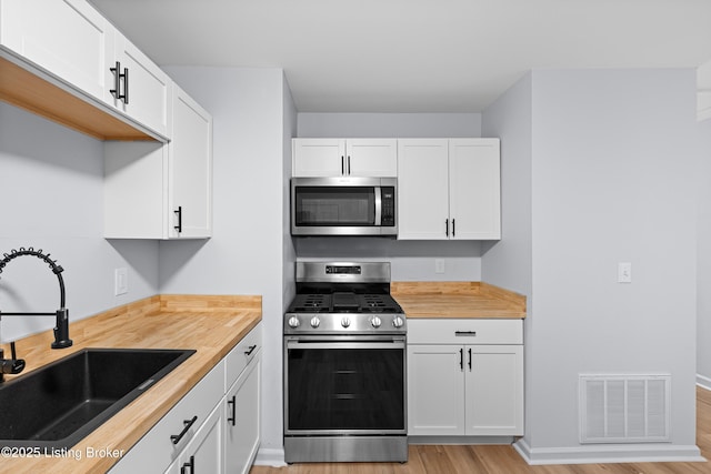 kitchen with appliances with stainless steel finishes, sink, white cabinets, and butcher block countertops