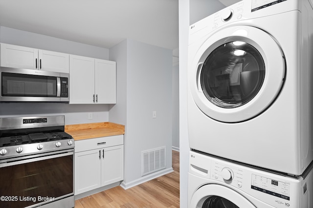 kitchen featuring stacked washer and dryer, white cabinetry, appliances with stainless steel finishes, and light hardwood / wood-style floors