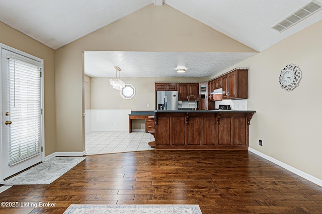 kitchen with kitchen peninsula, lofted ceiling, dark hardwood / wood-style floors, stainless steel fridge, and a kitchen breakfast bar