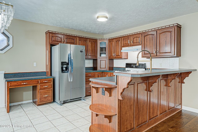 kitchen with kitchen peninsula, gas range, stainless steel refrigerator with ice dispenser, tasteful backsplash, and a textured ceiling