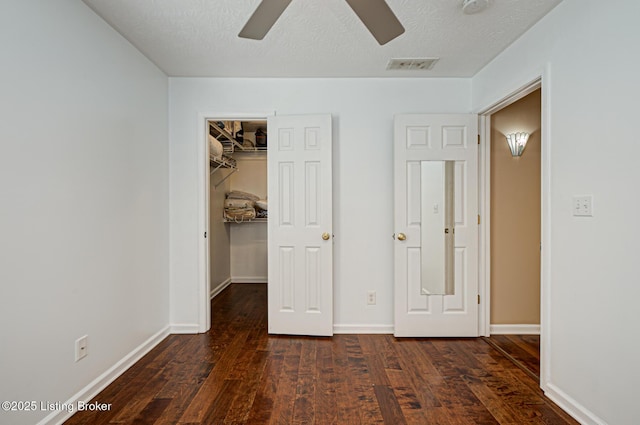 unfurnished bedroom with a textured ceiling, a closet, a walk in closet, and dark hardwood / wood-style flooring