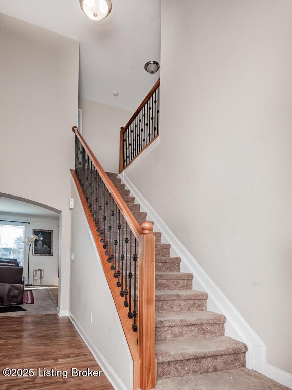 staircase with a high ceiling, wood finished floors, and baseboards