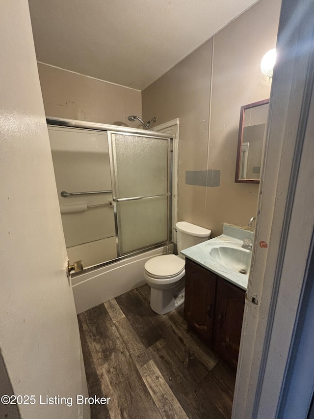 full bathroom with wood-type flooring, combined bath / shower with glass door, vanity, and toilet