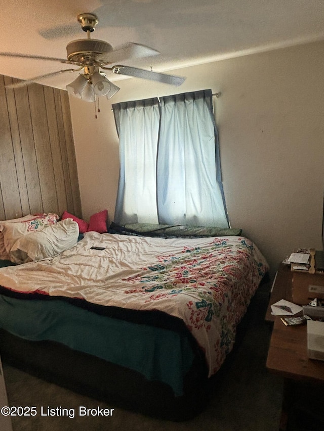 bedroom with ceiling fan and wood walls