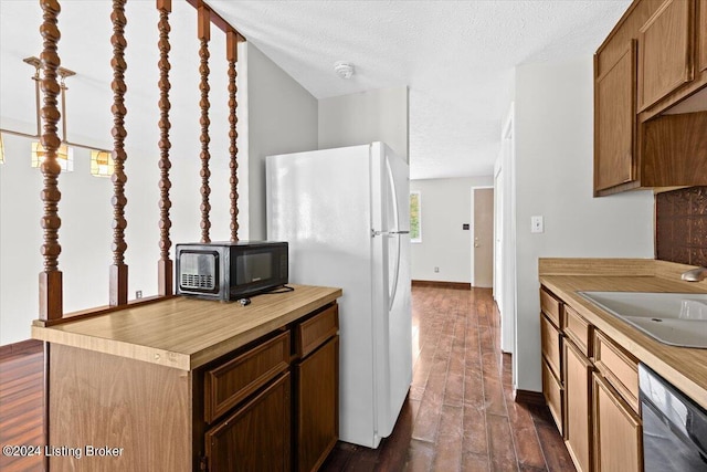 kitchen featuring dishwasher, sink, white refrigerator, dark wood-type flooring, and a textured ceiling